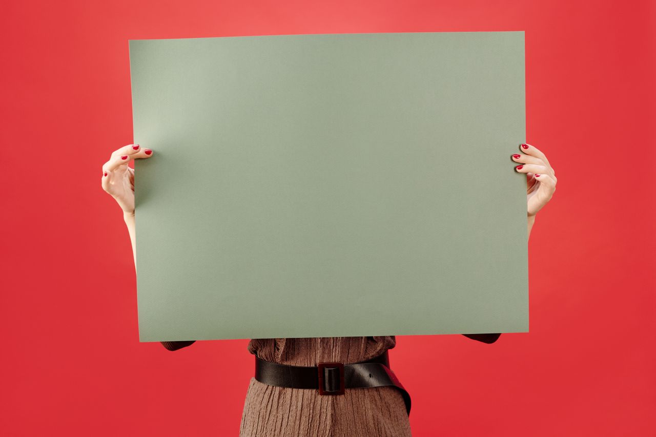 who-we-are Woman holds a blank poster board against vibrant red background, ideal for customization.