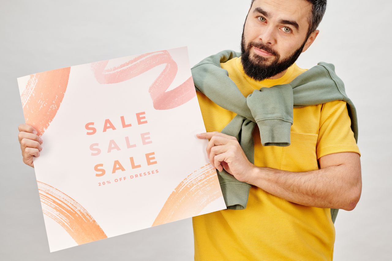 contact-hero Man holding a sale poster advertising 20% off dresses. Perfect for Black Friday promotions.