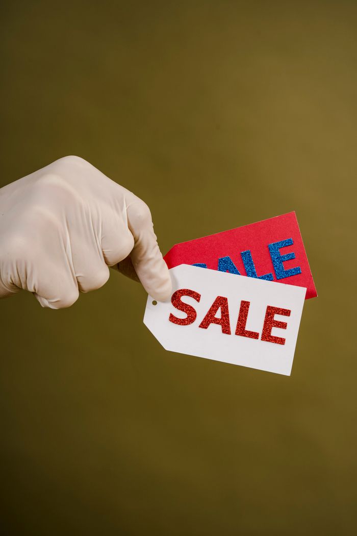 services-05 Gloved hand holding red and white sale tags on a green background, emphasizing shopping and discounts.