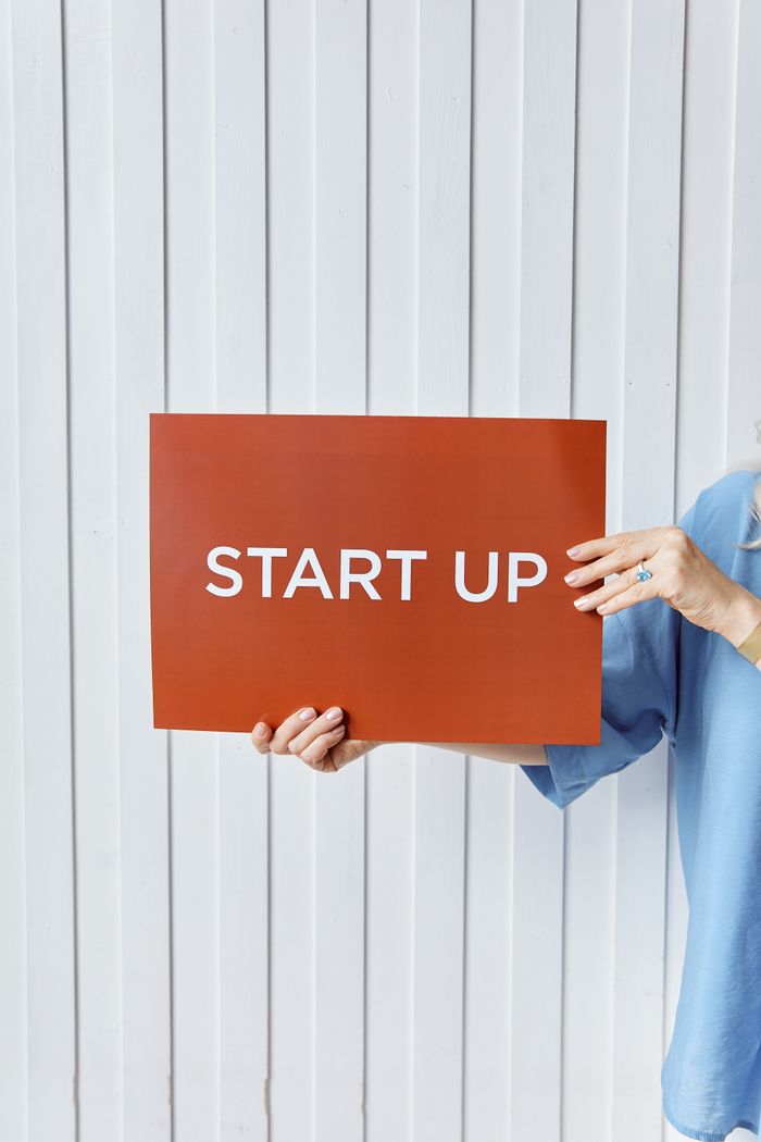 services-03 A person holding a sign reading 'START UP' against a white wooden backdrop.